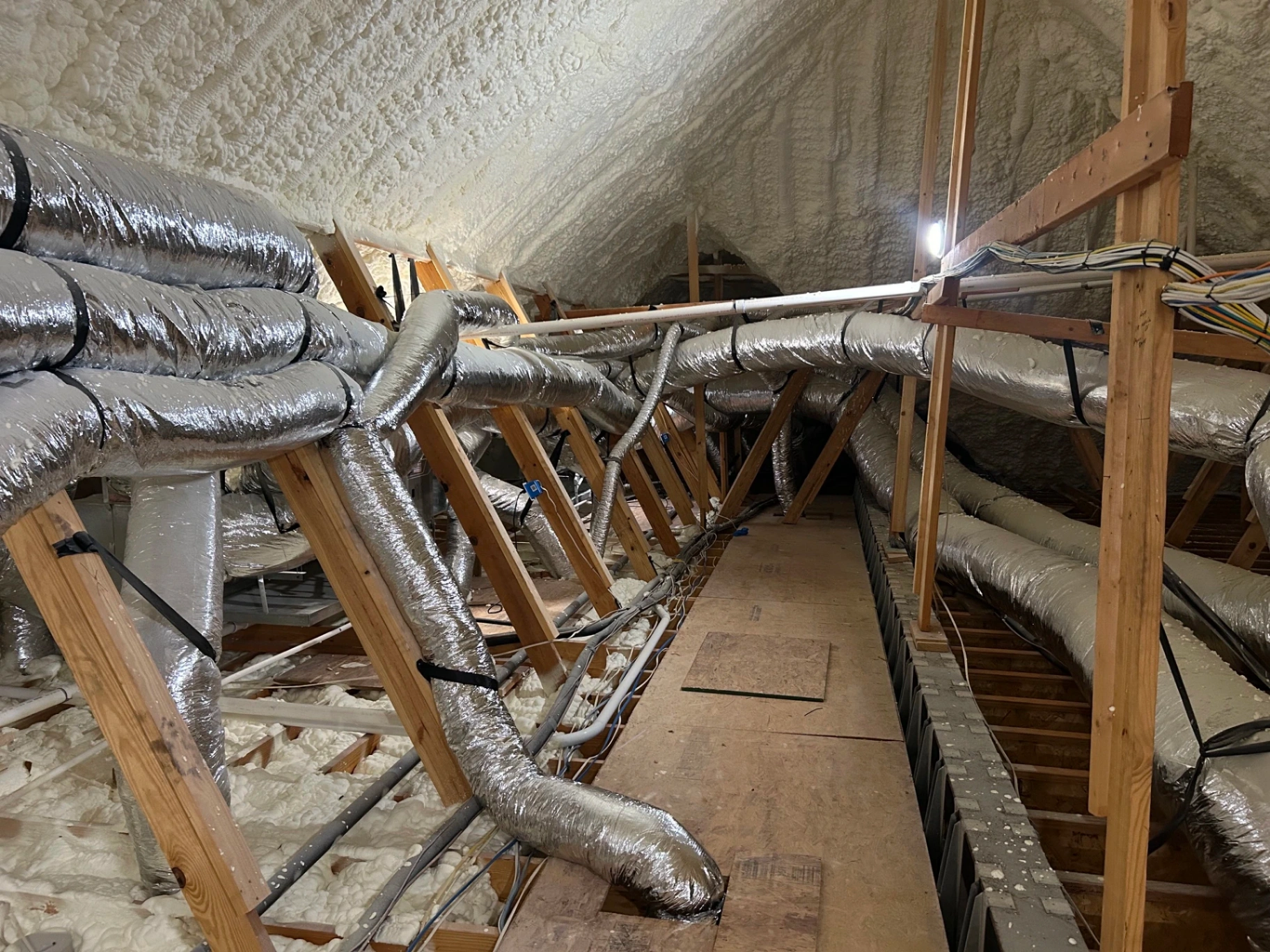 Insulated HVAC ductwork run through a spray-foamed residential attic