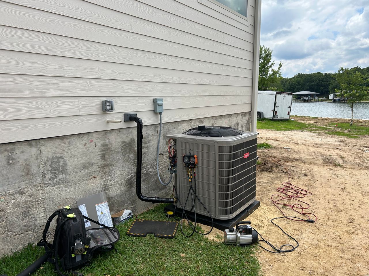 HVAC technician servicing AC unit with gauges at a lake house
